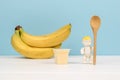 A figurine of a baby with a spoon, a glass of yogurt and a banana on a white table. The concept of healthy baby food Royalty Free Stock Photo