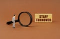 A figurine of a businesswoman looks through a magnifying glass at a block with the inscription - Staff Turnover