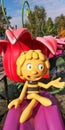Figurine of cartoon character Maya the Bee,sitting on purple petal in Holiday Park on sunny day against flower backdrop Royalty Free Stock Photo