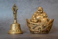 Figurine Cheerful Hotei and golden bell close-up, soothing and meditative. Smiling Buddha and golden bell Isolated on gray