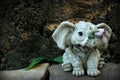 Figurine of a gray baby elephant in the garden on a path with yellow leaves