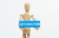 A figurine of a man holds in his hands a blue wooden block with the inscription ASTIGMATISM. The figure is out of focus Royalty Free Stock Photo