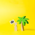 Figurine of a man with a poster with a bag under a palm tree on a yellow background. Travel agency. To meet new experiences