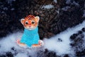A figurine of a toy tiger cub on the snow against a background of tree bark.