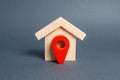 Figurine wooden house and red location pointer. The concept of the location of a building, surrounding infrastructure