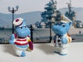 Figurines hippos of a sailor and a captain against the background of the seaport and a warship.