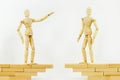 Figurines of man opposite each other stand on bridge divided by an abyss. man extends helping hand