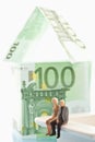 Figurines sitting in front of house of 100 Euro notes Royalty Free Stock Photo