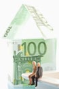 Figurines sitting in front of house of 100 Euro notes