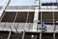 Filipino construction mason plastering grout on board scaffolding pipes on high-rise building alone