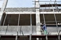 Filipino construction mason plastering grout on board scaffolding pipes on high-rise building alone