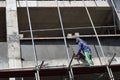 Filipino construction mason plastering grout on board scaffolding pipes on high-rise building alone