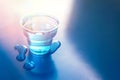 Filled blue glass of water on blue neon background with spilled water on it