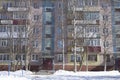 Filled frame full screen shot of an old ugly colorful facade of a soviet block house with windows, balconies and naked birches and