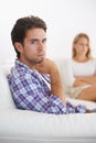Filled with frustration - relationship issues. A upset man sitting in a sofa with hand on chin and upset wife sitting in Royalty Free Stock Photo