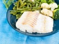 Fillet of boiled sea fish cod with broccoli, green beans and cauliflower on a blue plate, side view, close. Healthy diet dish for