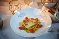 Fillet Of Grilled And Baked Codfish Served With Vegetables And Oil Sauce, On A Dish Next To Candles, A Glass Of Wine In