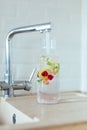 Filling a clear glass carafe with tap water. Water is infused with berries, mint and lemon Royalty Free Stock Photo