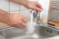 Filling a glass with tap water for drinking by holding it in man hand at the sink in the kitchen Royalty Free Stock Photo