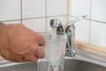 Filling a glass with tap water for drinking by holding it in man hand at the sink in the kitchen Royalty Free Stock Photo