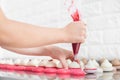 Filling macarons with ganache cream and fruit jam. Close up cropped shot of hands of female confectioner, squeezing red