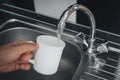 Filling white glass with tap water. Modern faucet and sink in home kitchen. Man pouring fresh drink to cup. Royalty Free Stock Photo