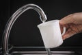 Filling white glass with tap water. Modern faucet and sink in home kitchen. pouring fresh drink cup on black background, housework Royalty Free Stock Photo