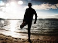 Film grain. Silhouette of person in sportswear and short hair on beach seeing into morning Sun above sea