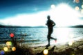 Film grain. Silhouette of tall sport active man running and exercising on beach at busch below sunset. Royalty Free Stock Photo