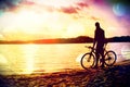 Film grain. Young man cyclist silhouette on blue sky and sunset background on the beach. End of season at lake. Royalty Free Stock Photo