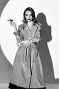 Film noir style: beautiful elegant woman smoking cigarette. Vintage retro portrait of charming young girl in trench coat. Black Royalty Free Stock Photo