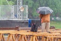 The filmmaker is filming the event in rainy weather hiding under an umbrella