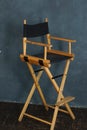 A filmmakers chair with wooden legs and a black seat stands against a gray-blue wall