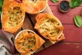 Filo pies with soft feta cheese and spinach in ceramic molds on old red wooden table backgrounds. Filo portions pies. Small Baked