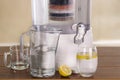 Filter system of water purifier with two glasses of water one filled until middle with a lemon inside and an empty