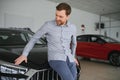 Final decision. Shot of a handsome young man standing in front of a new car at the dealership thinking rubbing his chin Royalty Free Stock Photo