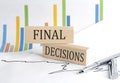 FINAL DECISIONS text on a wooden block on chart background , business concept