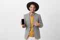 Finally new model of smartphone. Positive happy guy in stylish outfit and hat, showing smartphone and pointing at device Royalty Free Stock Photo