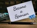 Phrase Become a sponsor written on white card with calculator,paper clip and a pen. Royalty Free Stock Photo