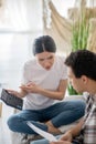 Brunette male holding papers, dark-haired female pointing at calculator, both sitting on sofa Royalty Free Stock Photo