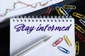 On the desktop are a forex chart, paper clips, a pen and a notebook in which it is written - Stay informed