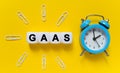 On a yellow background a blue alarm clock paper clips and white cubes on which the text is written - GAAS