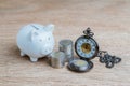 Finance or long term saving money and investment concept, white piggy bank and coins stacked and pocket watch on wood table Royalty Free Stock Photo