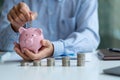 A businessman holds a piggy bank and puts coins in it for savings and business investments. Business risk and coin growth on the f