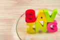 Empty glass jar piggy bank containing word SAVING on wooden desk