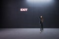 Find right decision and best way-out concept with pensive businesswoman back view in empty room looking at glowing neon exit sign Royalty Free Stock Photo