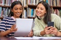 Find your thing. two females using their devices in a library. Royalty Free Stock Photo