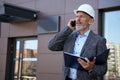 Finding solutions. Serious mature architect, engineer manager wearing helmet looking away, talking on the phone while Royalty Free Stock Photo