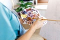 Fine art school. Closeup of artist hands holding wooden palette, mixing acrylic paint with brush.Artist woman with