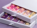 Fine chocolates bathed in pastel colors inside a white box. Violet background. Copy space.